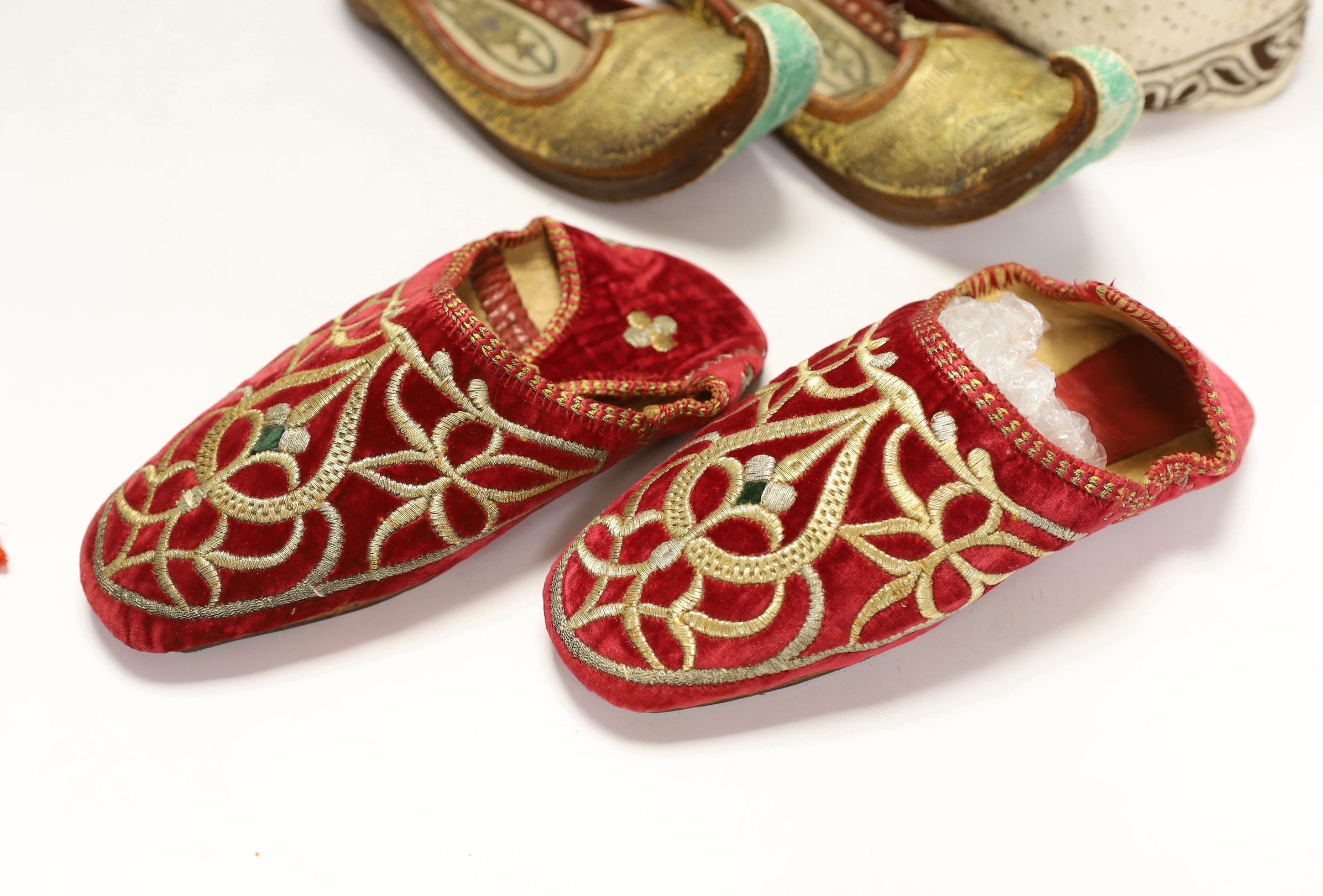 A pair of early 20th century metal thread embroidered Turkish slippers, a pair of similar embroidered red velvet children’s Indian slippers, an embroidered chain stitch drawstring purse and a quilted child’s hat